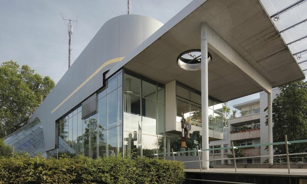 Architekturansicht des Museumsbaus Museum für Kommunikation Frankfurt
ein modernes Gebäude aus Metall, Beton und Glasmit einem überdachten Vorplatz. Auf dem Vorplatz vor der Frontscheibe steht eine Reiterstatue.