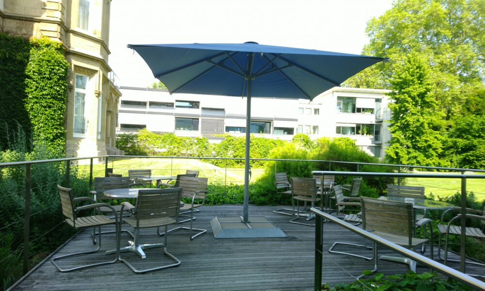 Cafe- Terasse mit Tischen, Stühle und einem aufgeklappten Sonnenschirm