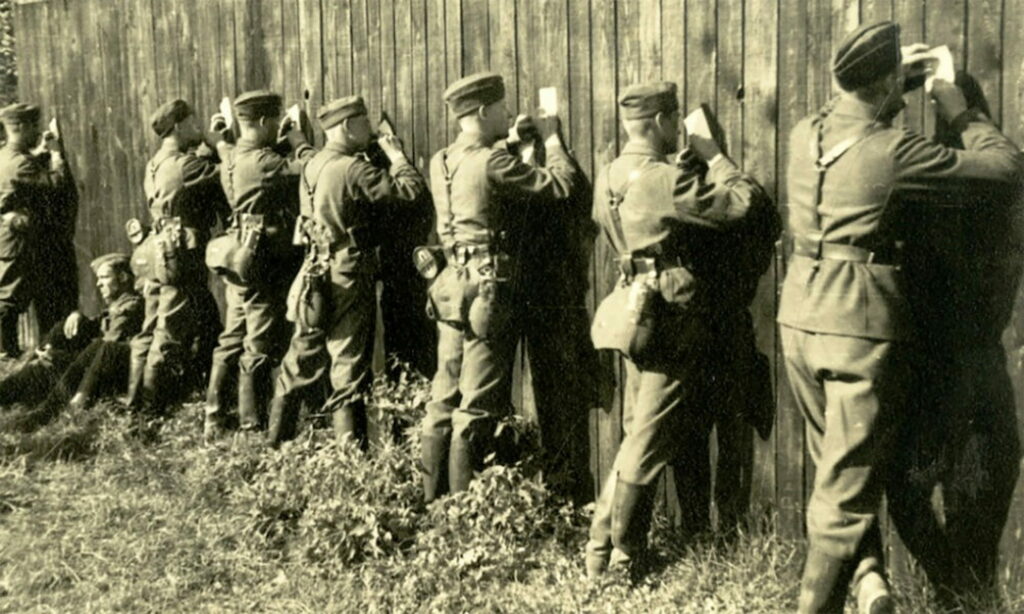 Acht Soldaten halten Papiere an die Wand und schreiben Briefe