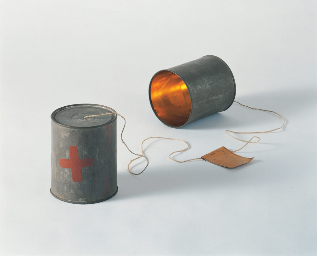 Das Fadentelefon von Joseph Beuys. Eine Dose steht und ist mit einem Stück Faden mit einer anderen Dose verbunden und bilden ein Dosentelefon.