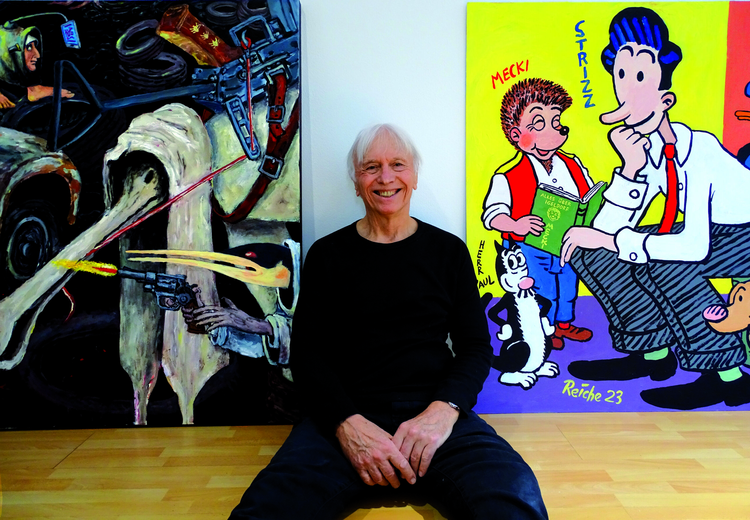 Volker Reiche sitzt zwischen zwei Gemälden auf dem Boden