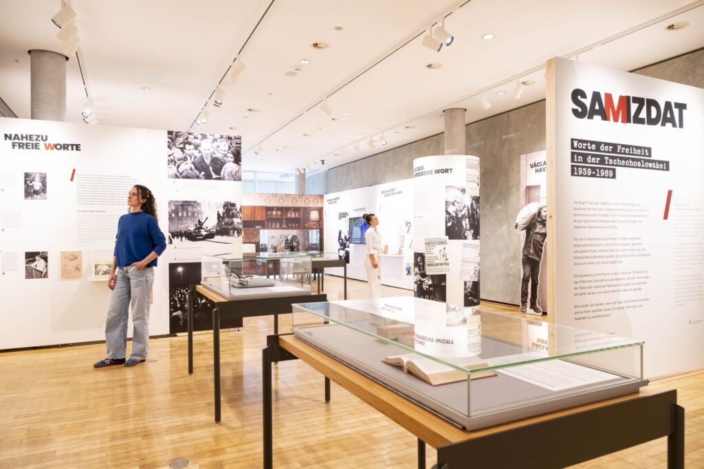 Besucher in einer Ausstellung mit Text- und Bildtafeln zur Geschichte von Samizdat und Literatur in der Tschechoslowakei.